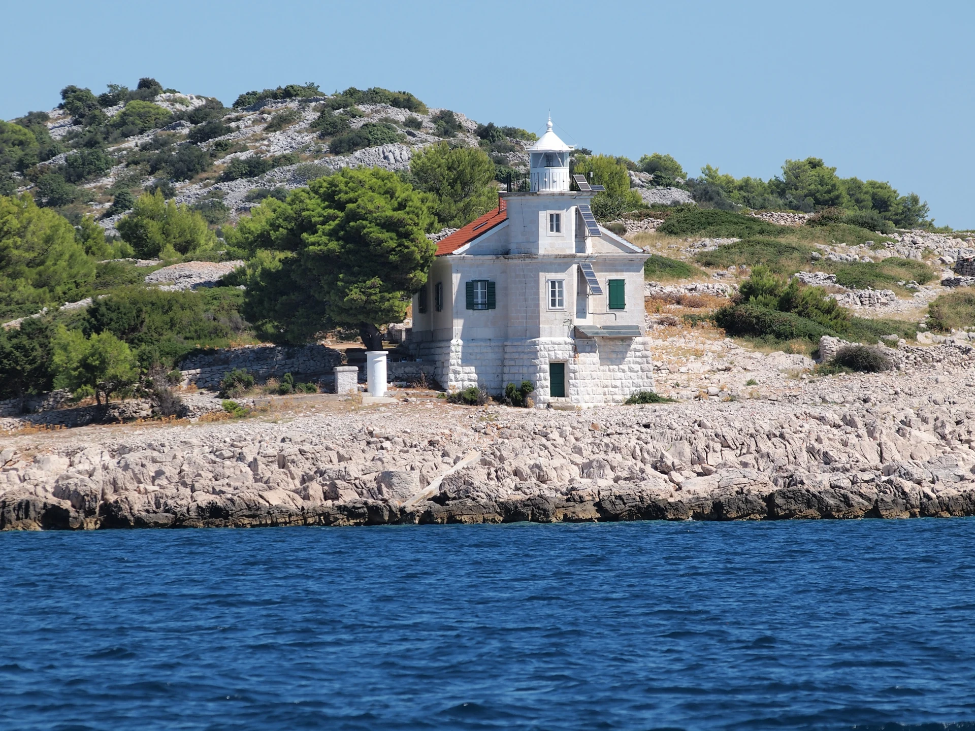 Prišnjak’s stone lighthouse above a rocky shore and pine trees